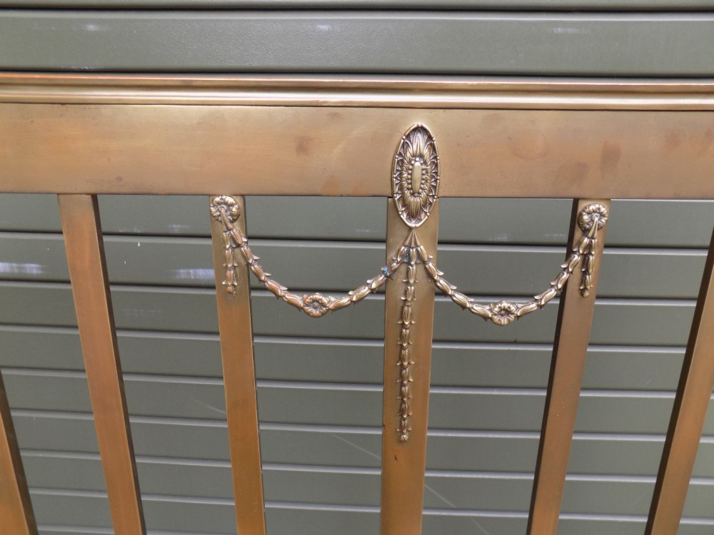 An antique Victorian brass bedstead with decorative urn finials, vertical spindles, ribbon swags, and castors. View VI