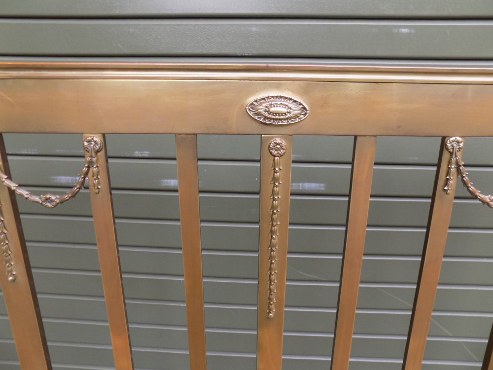 An antique Victorian brass bedstead with decorative urn finials, vertical spindles, ribbon swags, and castors. View VII