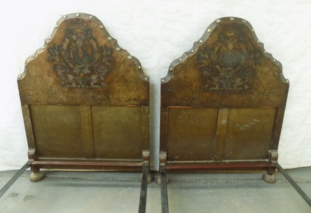 A pair of matching single bedsteads upholstered in aged brown hand-painted leather with brass stud trimming and arched tops. View II