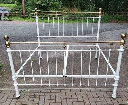 A white painted iron bedstead featuring vertical spindles, a horizontal top rail of polished brass, and brass ball finials.