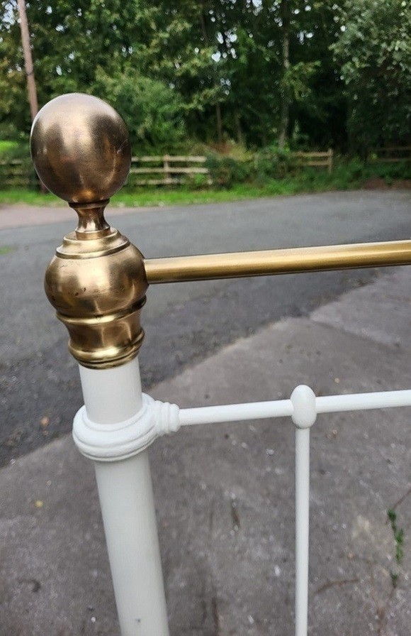 A white painted iron bedstead featuring vertical spindles, a horizontal top rail of polished brass, and brass ball finials. View II