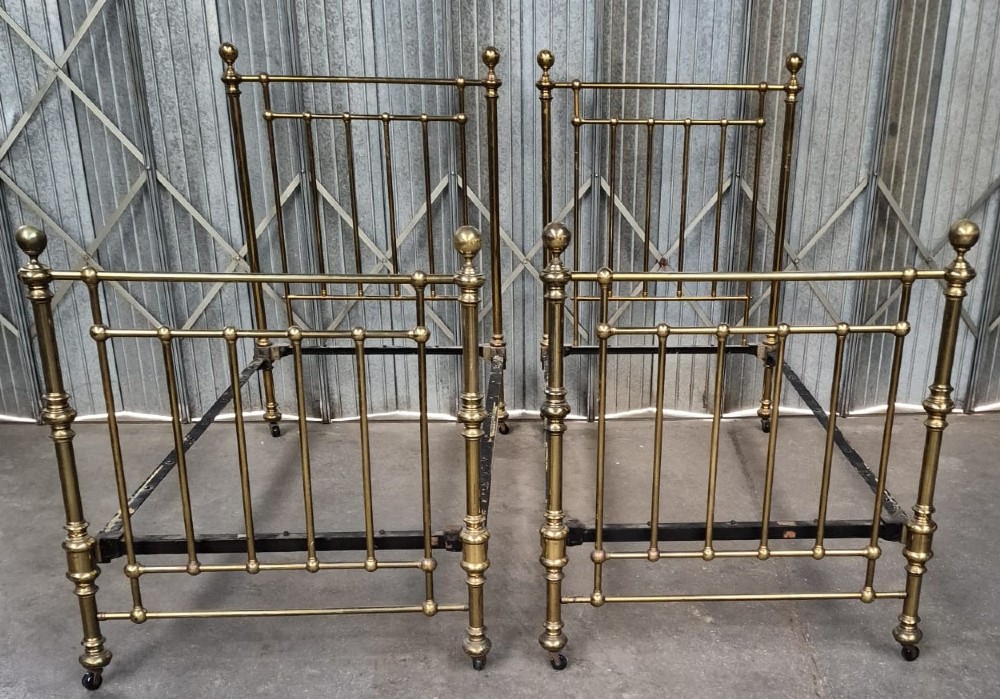 A pair of matching Victorian brass single bedsteads featuring vertical tubular spindles, ball finials, and castors.