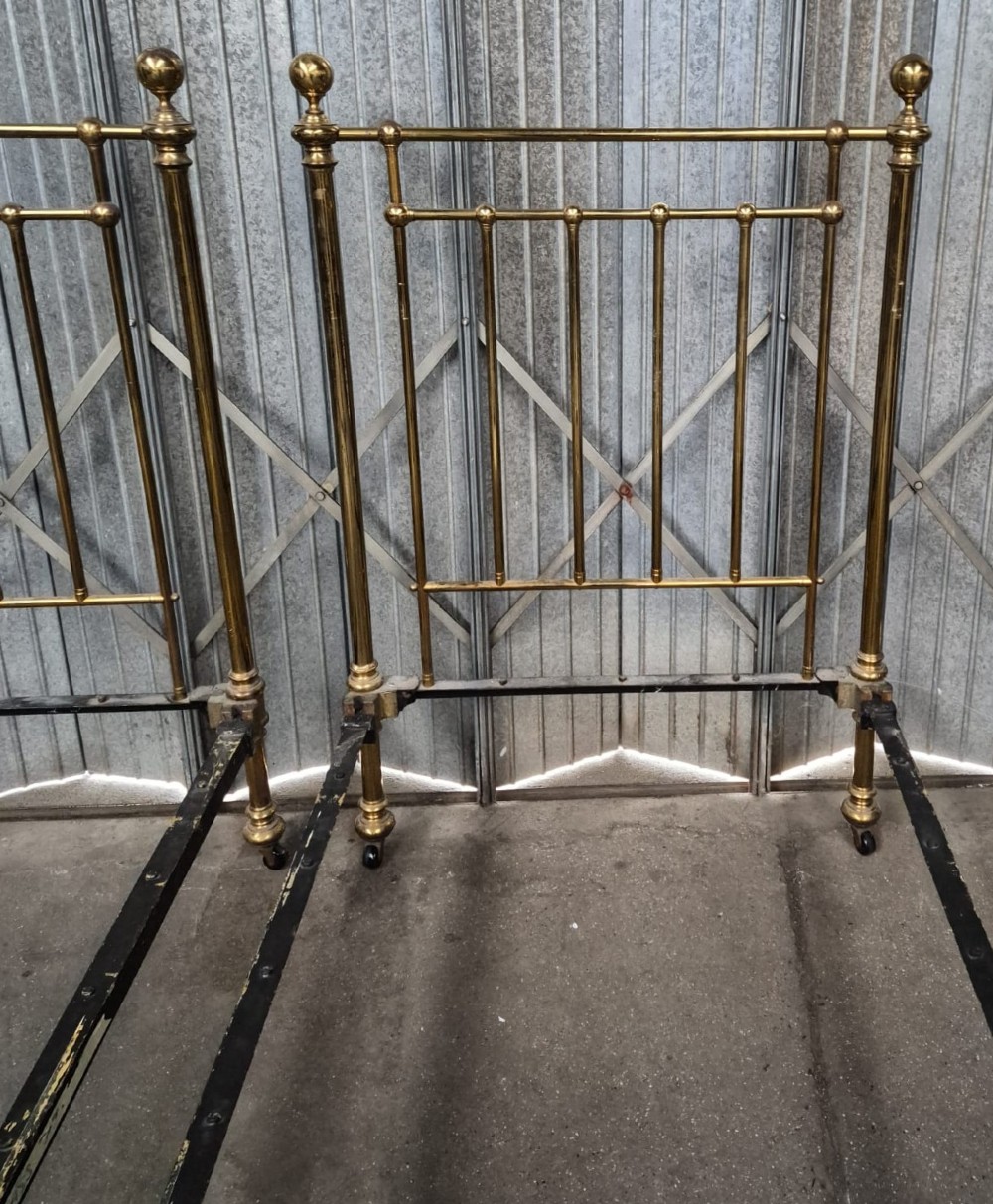 A pair of matching Victorian brass single bedsteads featuring vertical tubular spindles, ball finials, and castors. View II