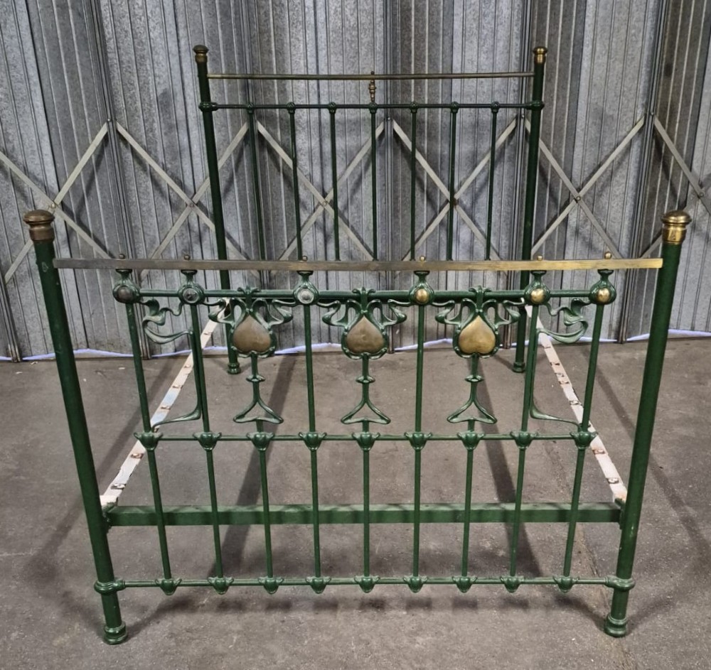 A Victorian Art Nouveau double bedstead featuring dark green painted iron frames, stylized heart-shaped motifs, and brass top rails with finials.