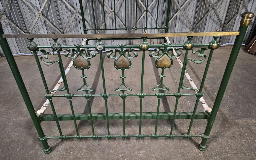 A Victorian Art Nouveau double bedstead featuring dark green painted iron frames, stylized heart-shaped motifs, and brass top rails with finials. View III