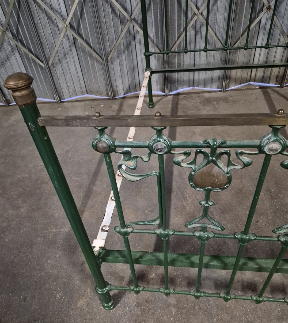 A Victorian Art Nouveau double bedstead featuring dark green painted iron frames, stylized heart-shaped motifs, and brass top rails with finials. View V