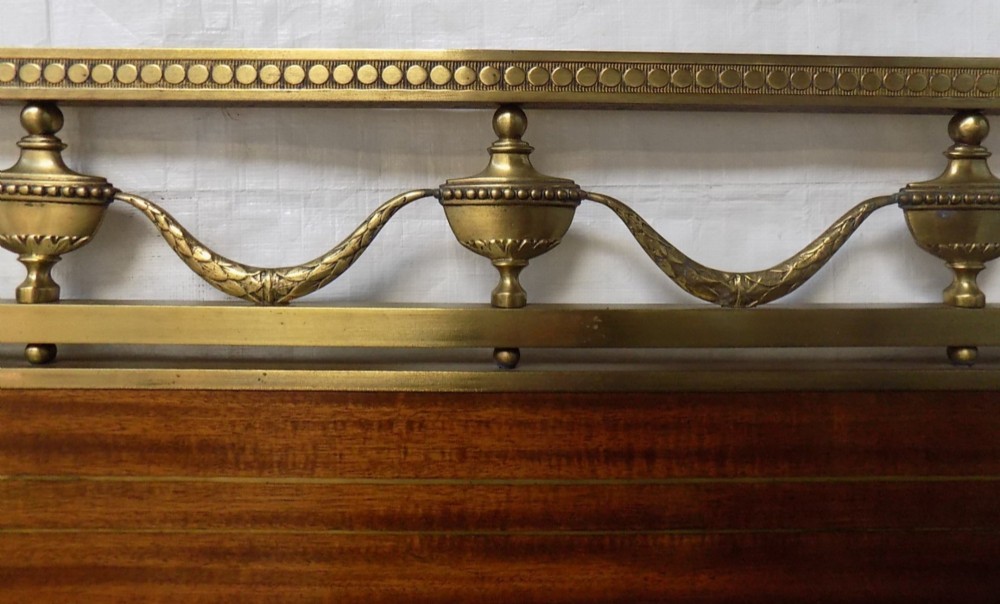 A pair of late Victorian brass-framed twin bedsteads featuring polished brass rails, top drapery swags, urn finials, and central mahogany timber panels with decorative brass plaques. View VI