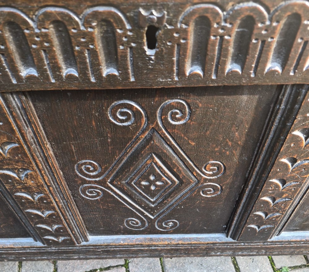 A dark carved oak coffer featuring a three-panel front with carved diamond lozenge patterns and an arcaded top rail. View V