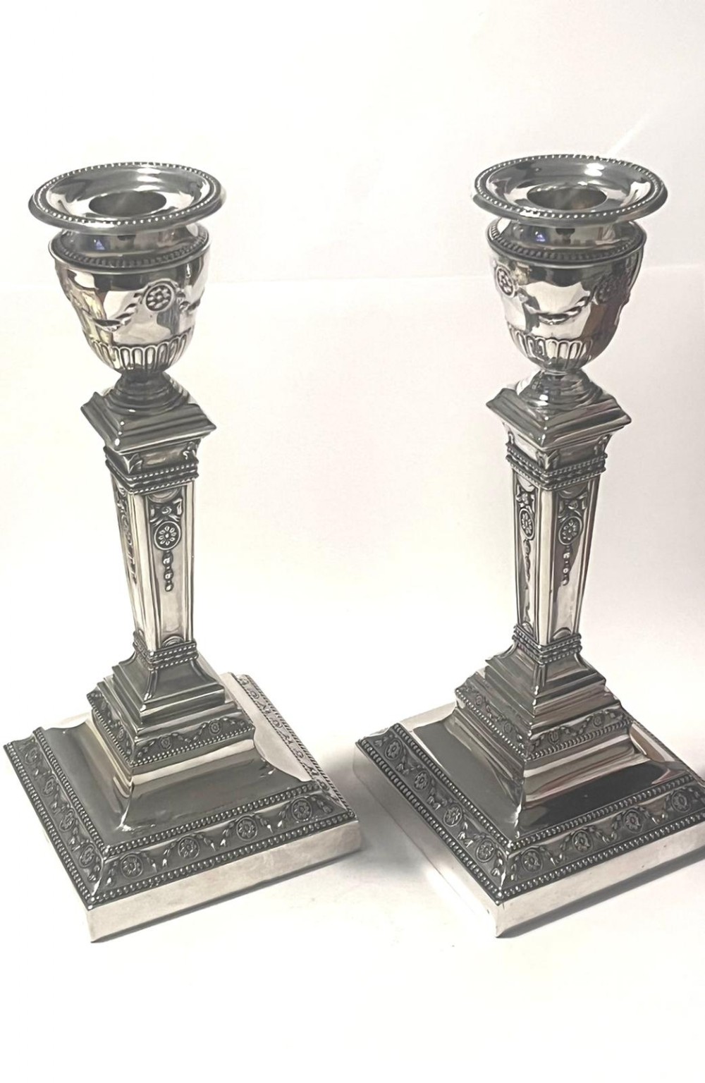 A pair of silver Edwardian candlesticks featuring urn-shaped sconces, relief swag ornamentation, and square stepped bases.