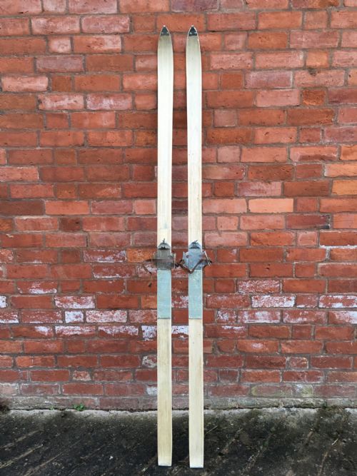 fig 1. A pair of tall light-coloured wooden skis featuring metal bindings and leather straps positioned vertically.