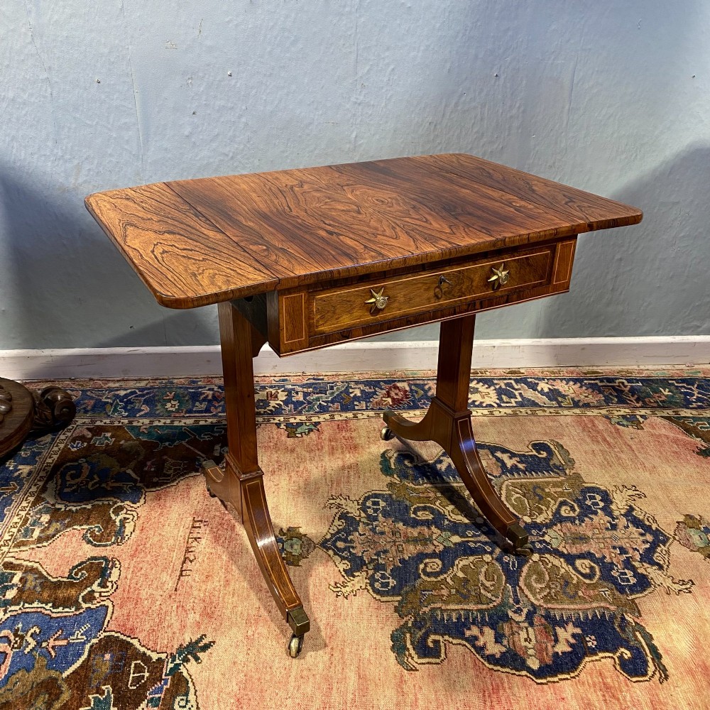 A George III rosewood drop-leaf sofa table with a single drawer, twin brass star handles, and splayed legs on brass castors.