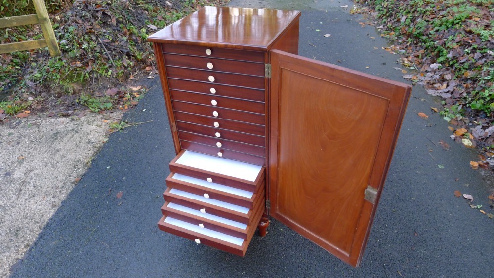 A nineteenth-century mahogany collectors cabinet featuring an open panelled door revealing multiple shallow drawers with light-coloured knob handles. View IX