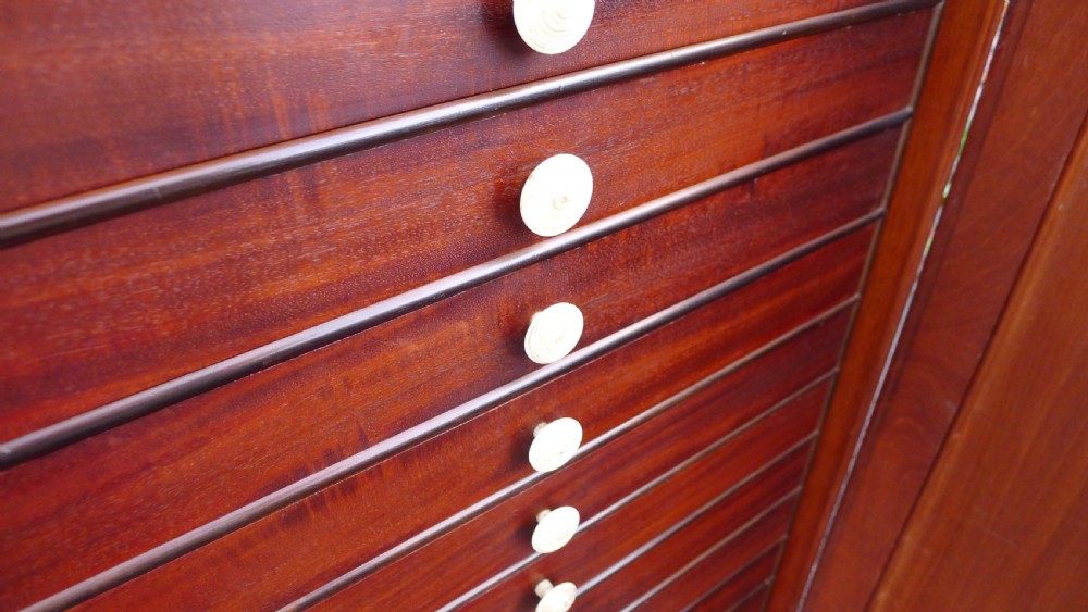 A nineteenth-century mahogany collectors cabinet featuring an open panelled door revealing multiple shallow drawers with light-coloured knob handles. View X