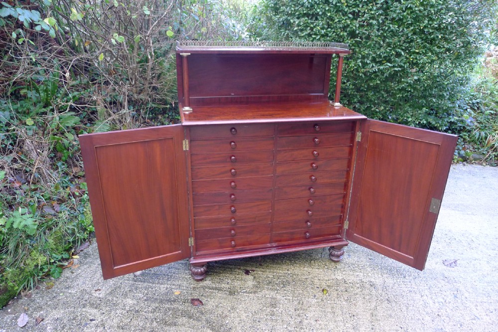 Victorian flame mahogany collectors cabinet featuring an upper shelf with a brass gallery and double doors opening to reveal multiple shallow drawers. View II