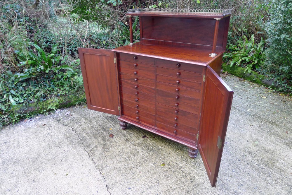 Victorian flame mahogany collectors cabinet featuring an upper shelf with a brass gallery and double doors opening to reveal multiple shallow drawers. View III