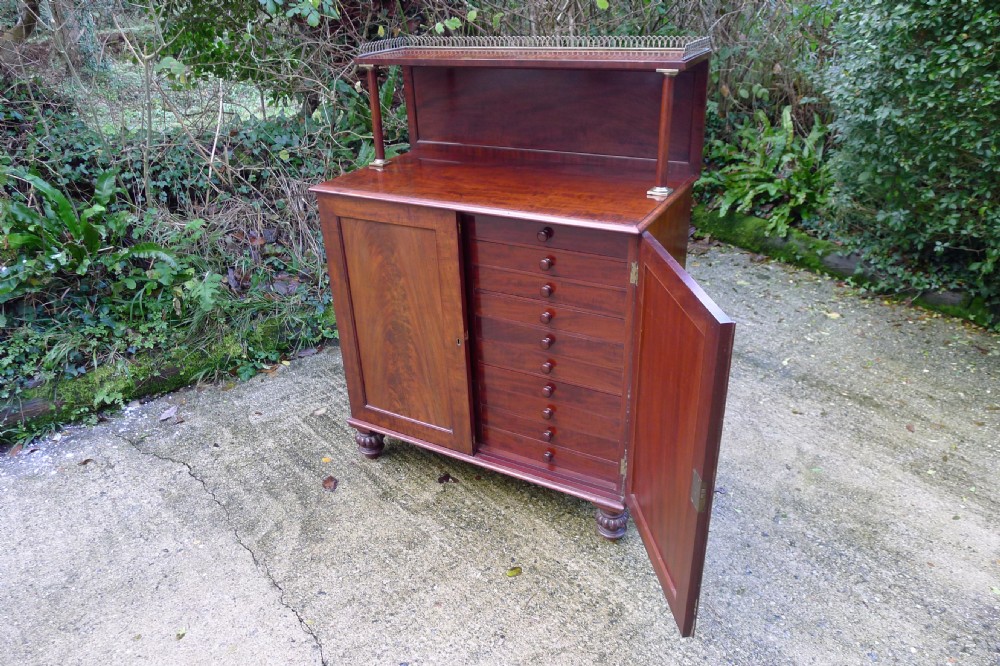 Victorian flame mahogany collectors cabinet featuring an upper shelf with a brass gallery and double doors opening to reveal multiple shallow drawers. View VII