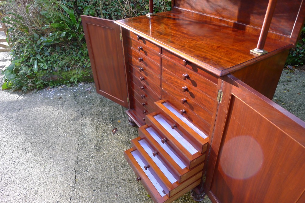 Victorian flame mahogany collectors cabinet featuring an upper shelf with a brass gallery and double doors opening to reveal multiple shallow drawers. View XXI