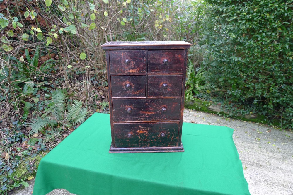 A small dark-stained deal wood collectors cabinet featuring six drawers with turned wooden knobs.