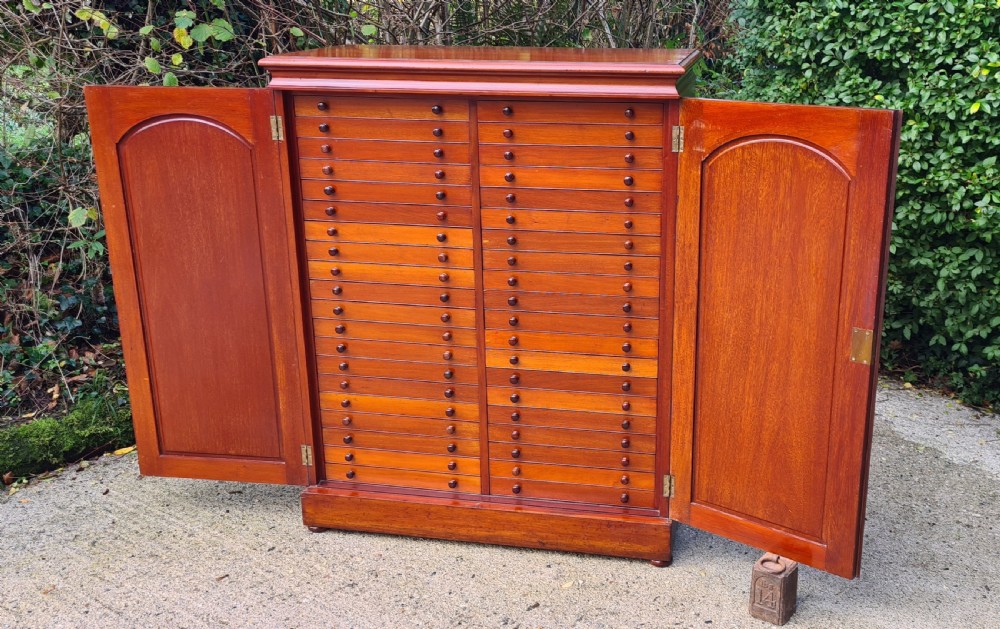 An Edwardian mahogany collectors cabinet with double doors open to reveal forty shallow drawers with small turned wooden knobs, featuring one drawer pulled forward displaying a glass cover. View V