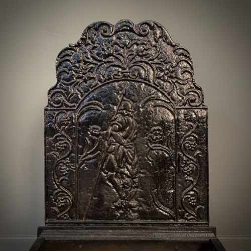 fig 1. A black cast and wrought iron fire basket featuring a relief-decorated fireback, slatted log holder, scrolled iron side supports, and polished brass ball finials.