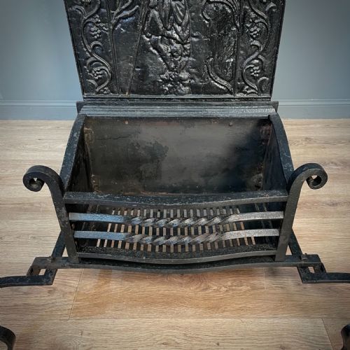 fig 3. A black cast and wrought iron fire basket featuring a relief-decorated fireback, slatted log holder, scrolled iron side supports, and polished brass ball finials.