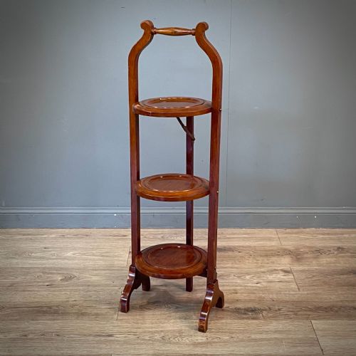 fig 2. An antique three-tier folding mahogany cake stand with circular platforms, a top carrying handle, and splayed feet.