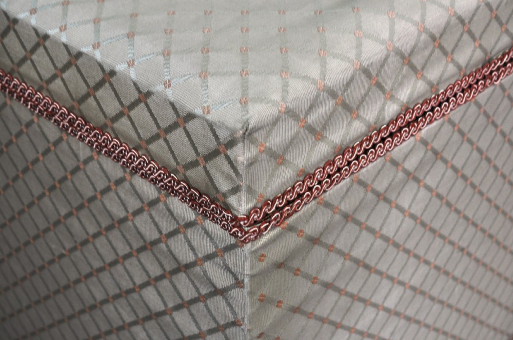 A rectangular Victorian blanket box upholstered in cream lattice-patterned fabric featuring terracotta braid trim around the lid edge. View XII