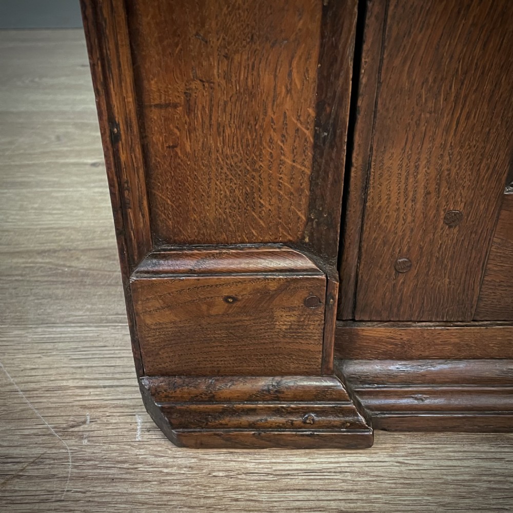 An antique Georgian oak hanging corner cabinet featuring an arched panel door, moulded top cornice, and brass fittings. View VI