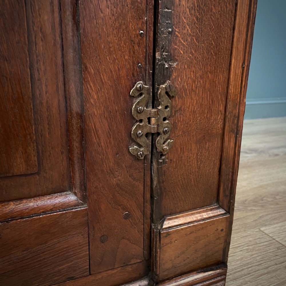 An antique Georgian oak hanging corner cabinet featuring an arched panel door, moulded top cornice, and brass fittings. View VII