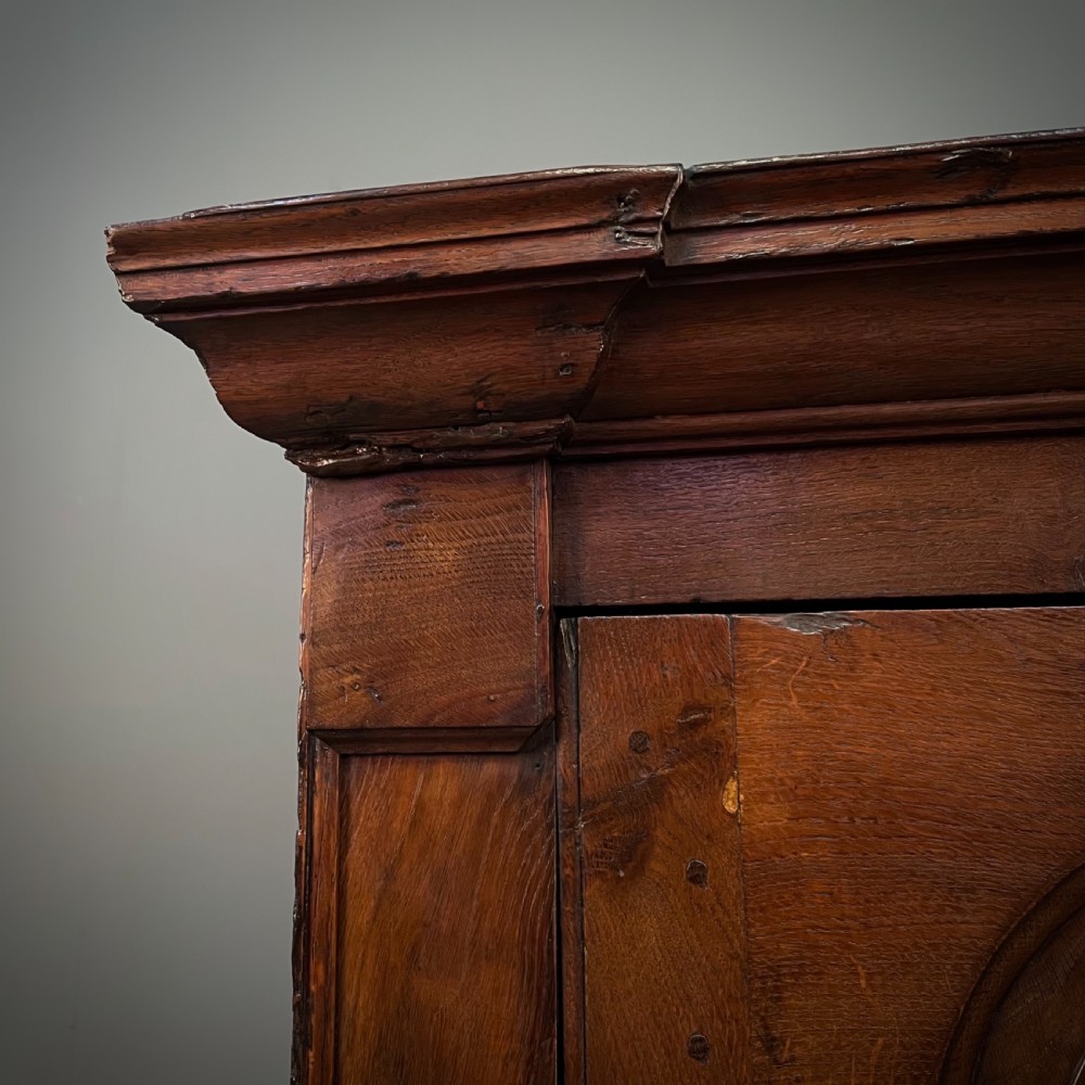 An antique Georgian oak hanging corner cabinet featuring an arched panel door, moulded top cornice, and brass fittings. View VIII
