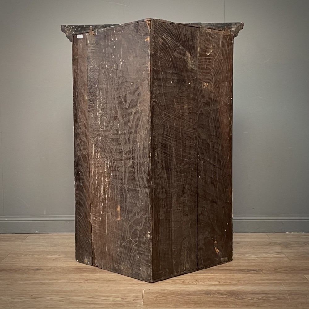 An antique Georgian oak hanging corner cabinet featuring an arched panel door, moulded top cornice, and brass fittings. View XI
