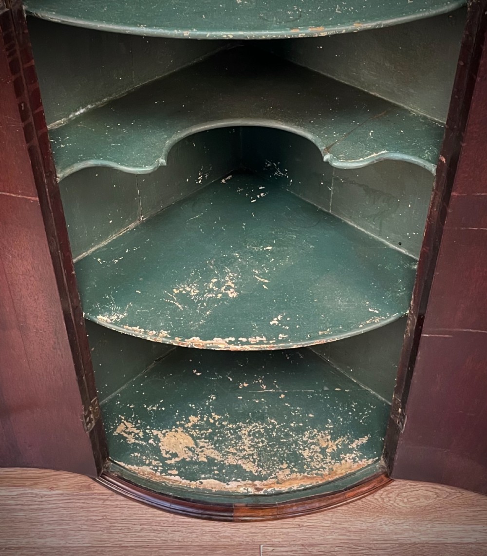 A Georgian mahogany bow-front hanging corner cabinet featuring double doors with flame timber grain, brass escutcheon, and a dentil-moulded top cornice. View V