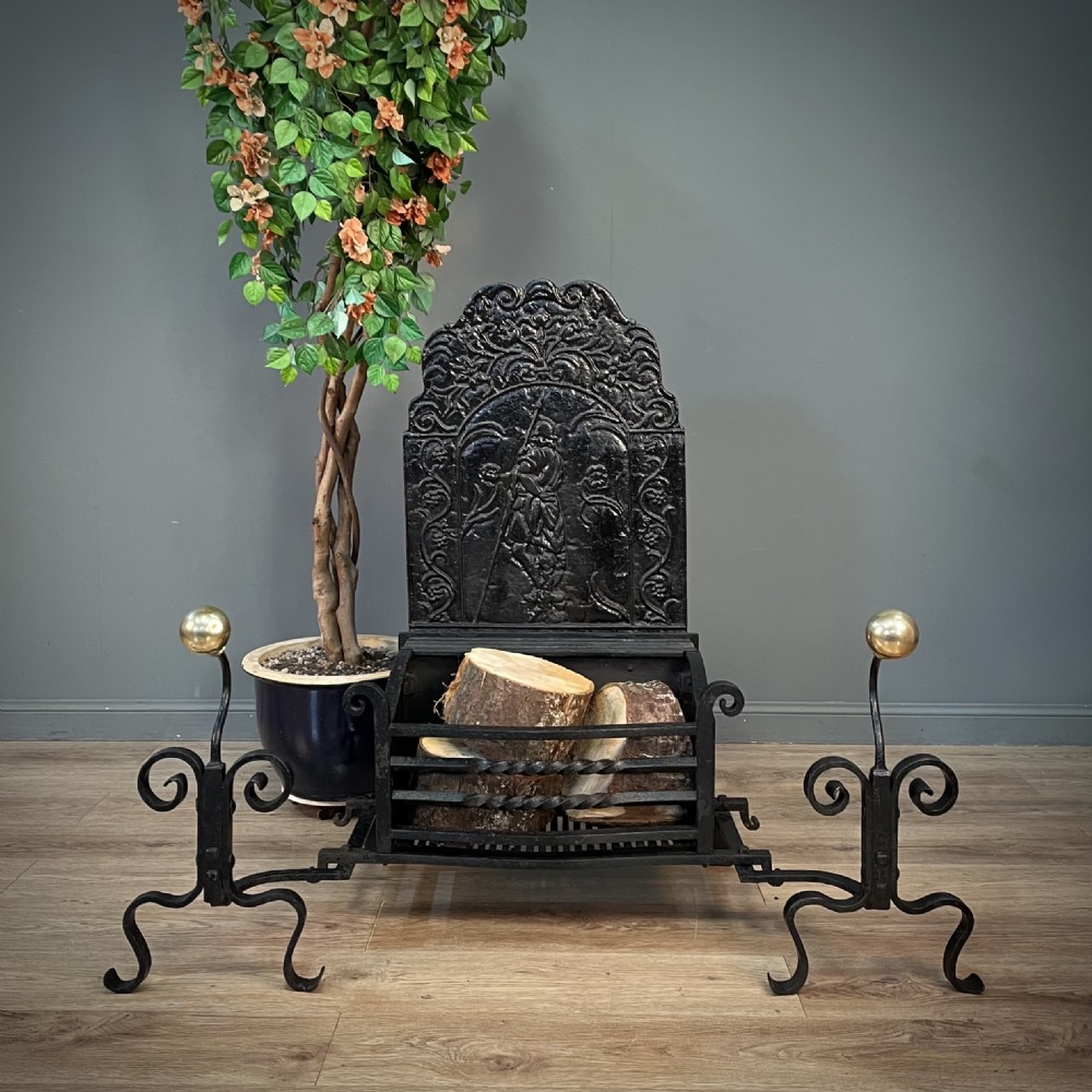 A black cast and wrought iron fire basket featuring a relief-decorated fireback, slatted log holder, scrolled iron side supports, and polished brass ball finials.