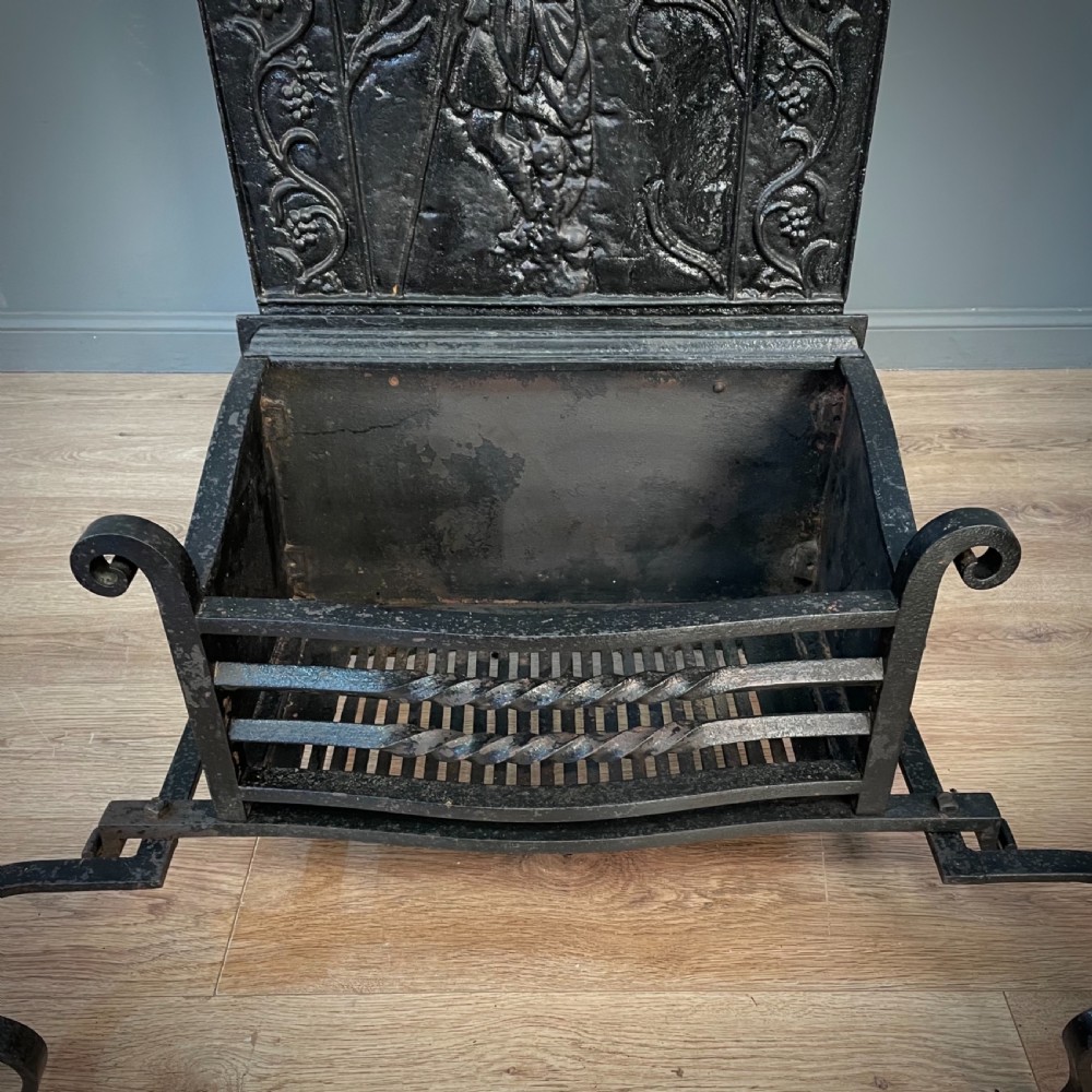 A black cast and wrought iron fire basket featuring a relief-decorated fireback, slatted log holder, scrolled iron side supports, and polished brass ball finials. View IV