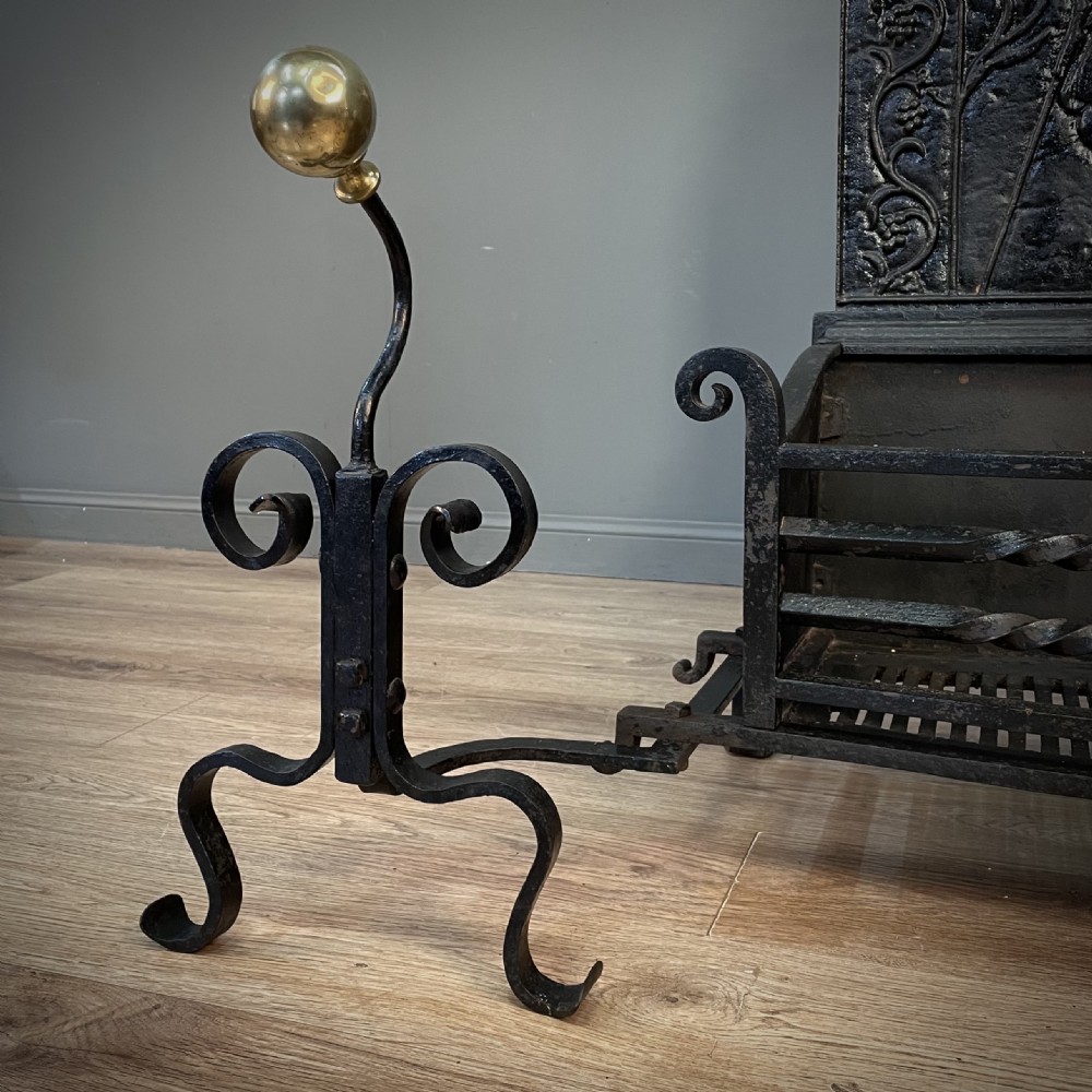 A black cast and wrought iron fire basket featuring a relief-decorated fireback, slatted log holder, scrolled iron side supports, and polished brass ball finials. View V