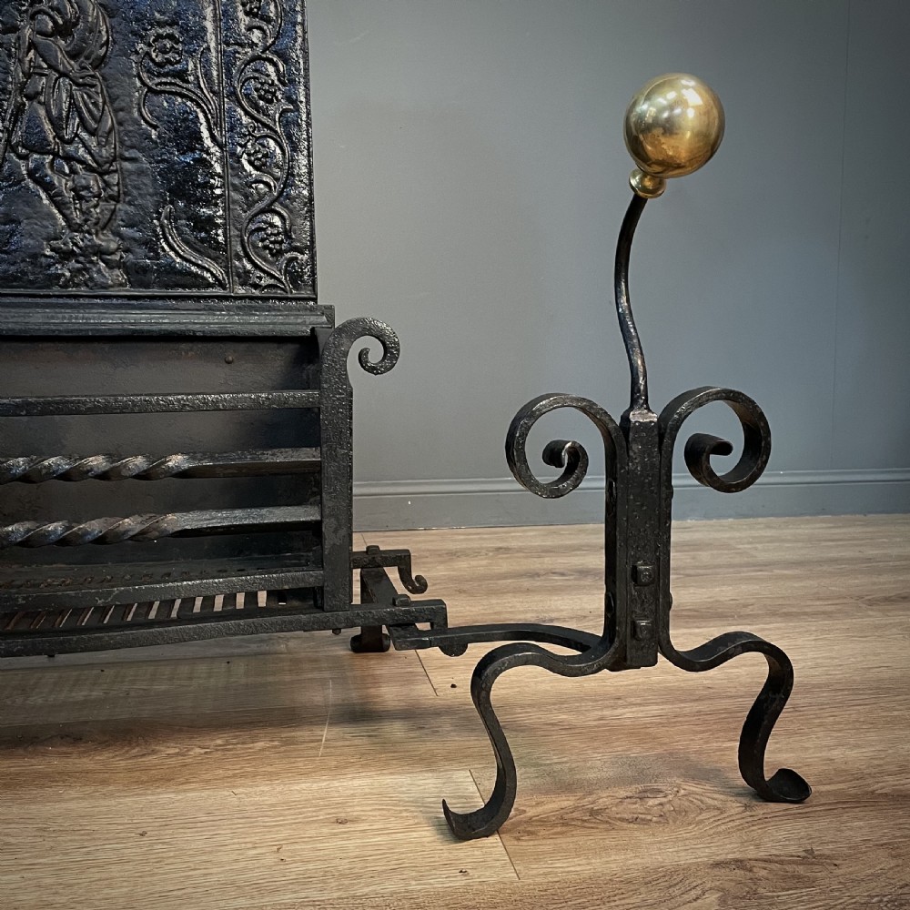 A black cast and wrought iron fire basket featuring a relief-decorated fireback, slatted log holder, scrolled iron side supports, and polished brass ball finials. View VI