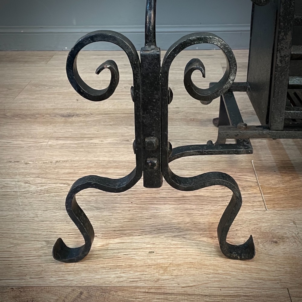 A black cast and wrought iron fire basket featuring a relief-decorated fireback, slatted log holder, scrolled iron side supports, and polished brass ball finials. View X
