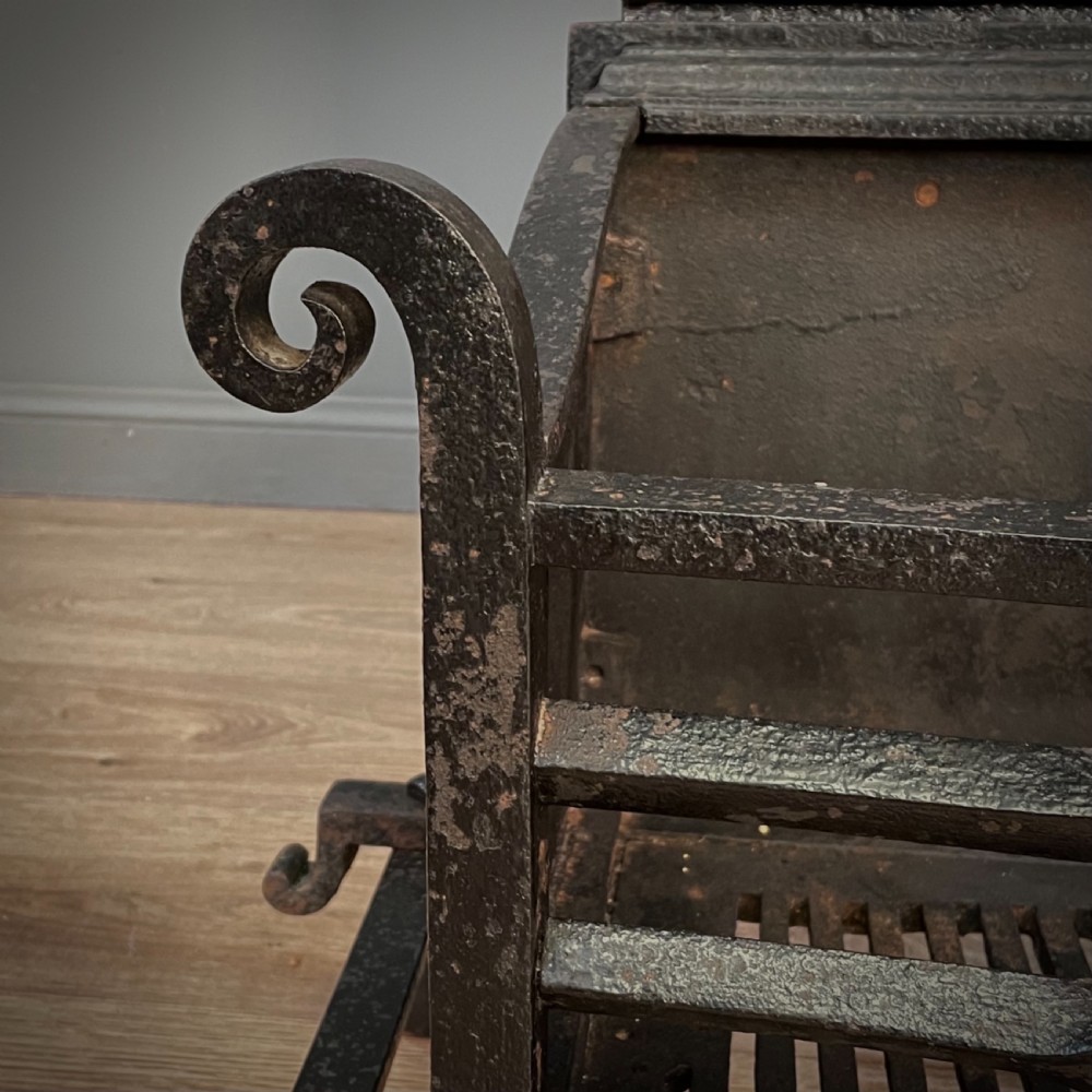A black cast and wrought iron fire basket featuring a relief-decorated fireback, slatted log holder, scrolled iron side supports, and polished brass ball finials. View XI