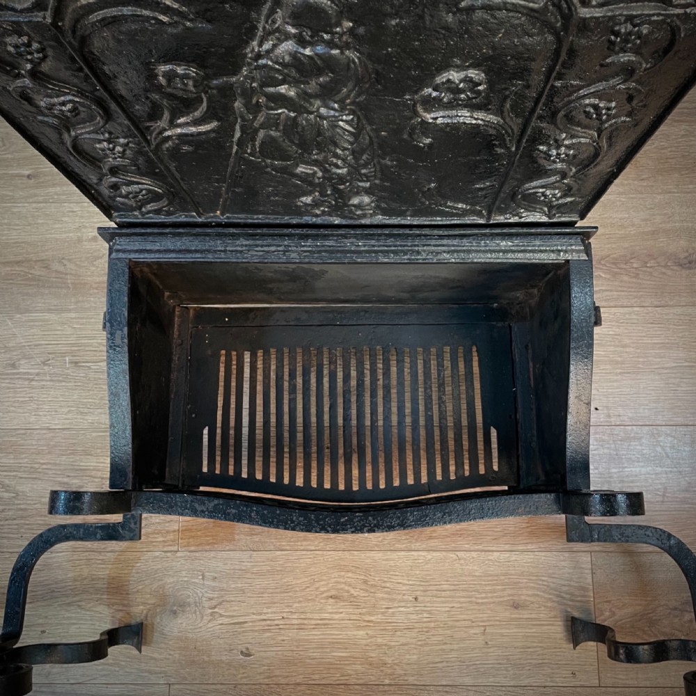 A black cast and wrought iron fire basket featuring a relief-decorated fireback, slatted log holder, scrolled iron side supports, and polished brass ball finials. View XIV