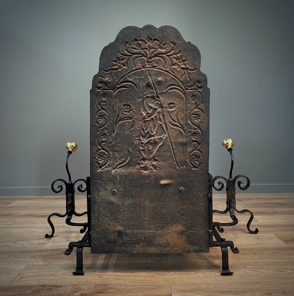 A black cast and wrought iron fire basket featuring a relief-decorated fireback, slatted log holder, scrolled iron side supports, and polished brass ball finials. View XV