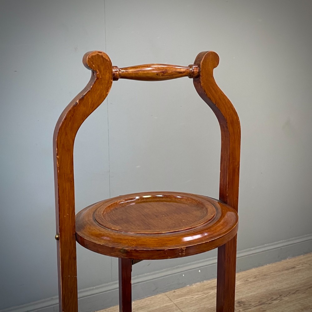 An antique three-tier folding mahogany cake stand with circular platforms, a top carrying handle, and splayed feet. View II