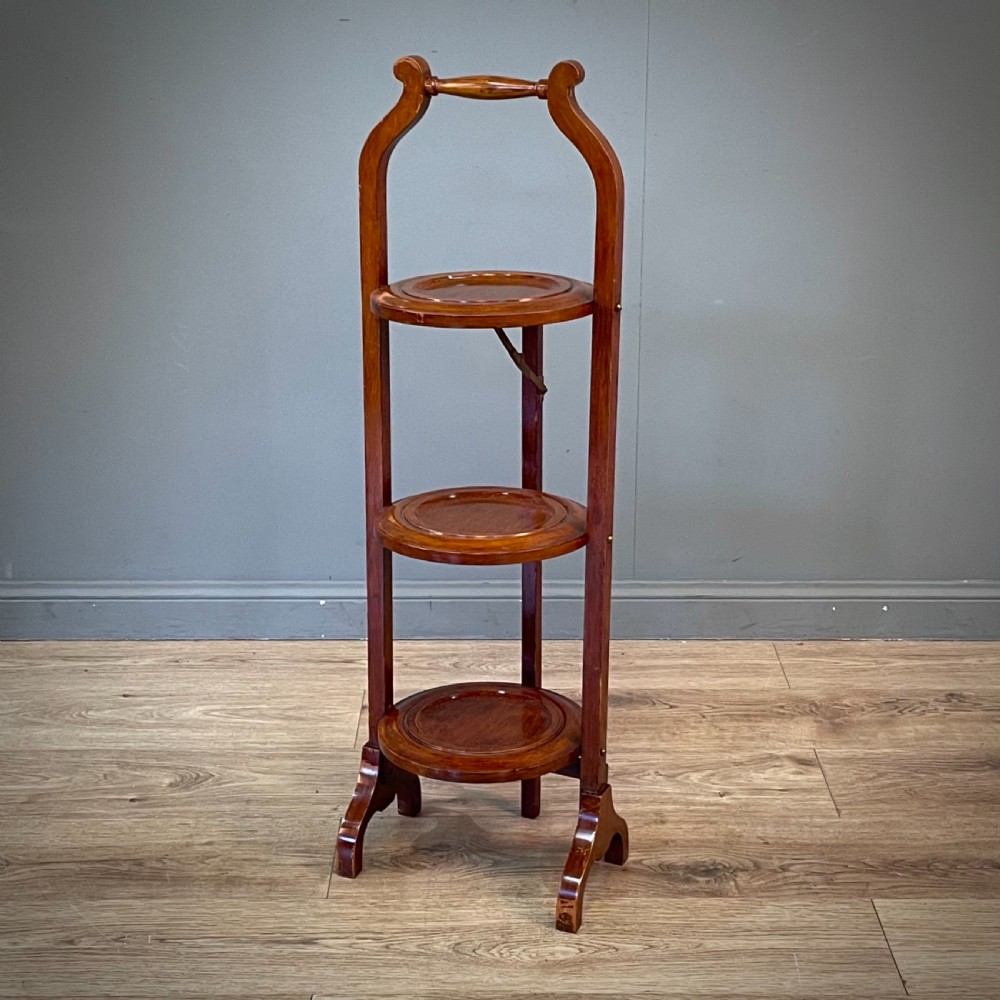 An antique three-tier folding mahogany cake stand with circular platforms, a top carrying handle, and splayed feet. View III