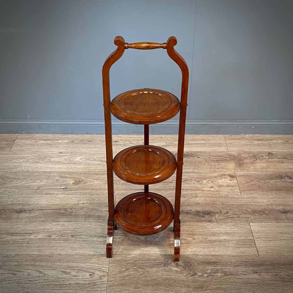 An antique three-tier folding mahogany cake stand with circular platforms, a top carrying handle, and splayed feet. View IV