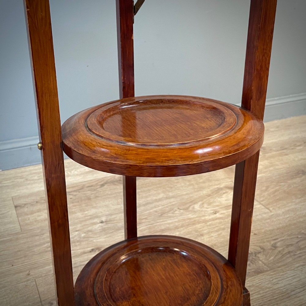 An antique three-tier folding mahogany cake stand with circular platforms, a top carrying handle, and splayed feet. View V