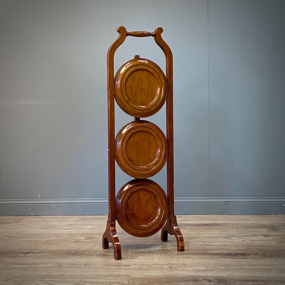 An antique three-tier folding mahogany cake stand with circular platforms, a top carrying handle, and splayed feet. View VI