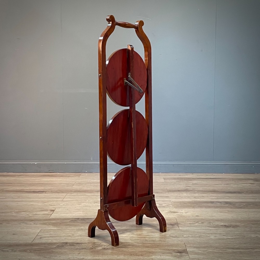 An antique three-tier folding mahogany cake stand with circular platforms, a top carrying handle, and splayed feet. View VIII