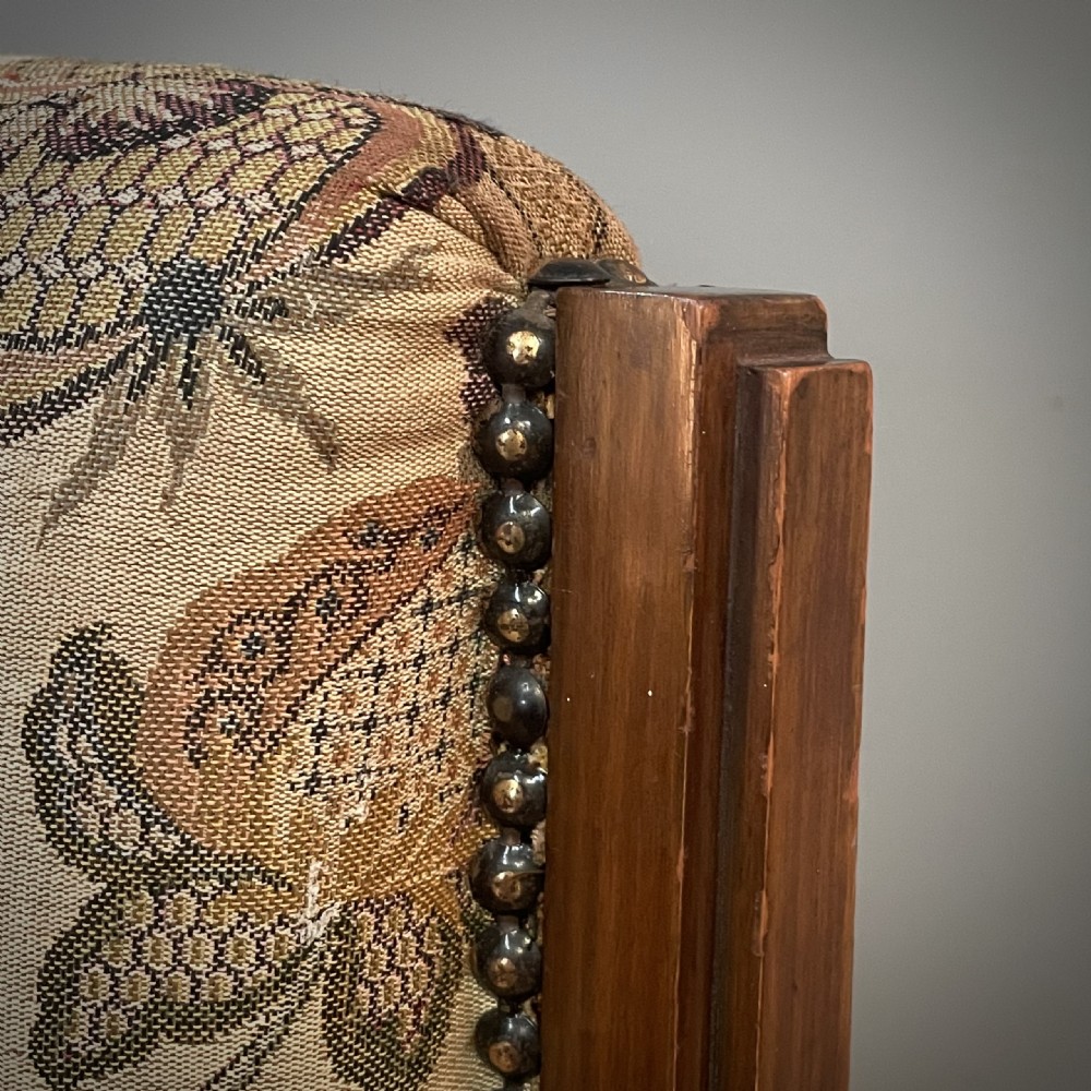 An antique walnut nursing chair featuring a tall rectangular backrest, floral upholstery, stud trim, and tapered wooden legs. View VI