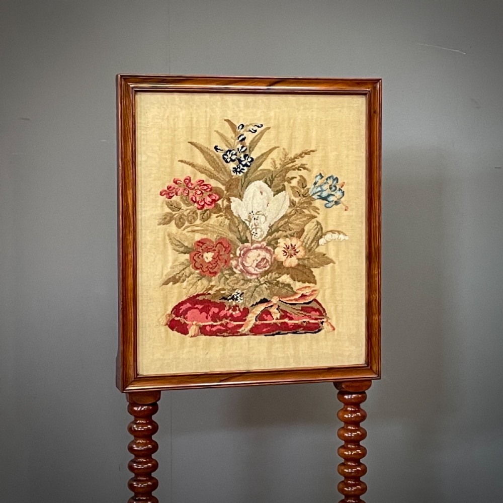 A Victorian mahogany fire screen featuring bobbin-turned uprights, carved feet, and a framed needlework panel displaying a floral bouquet. View II