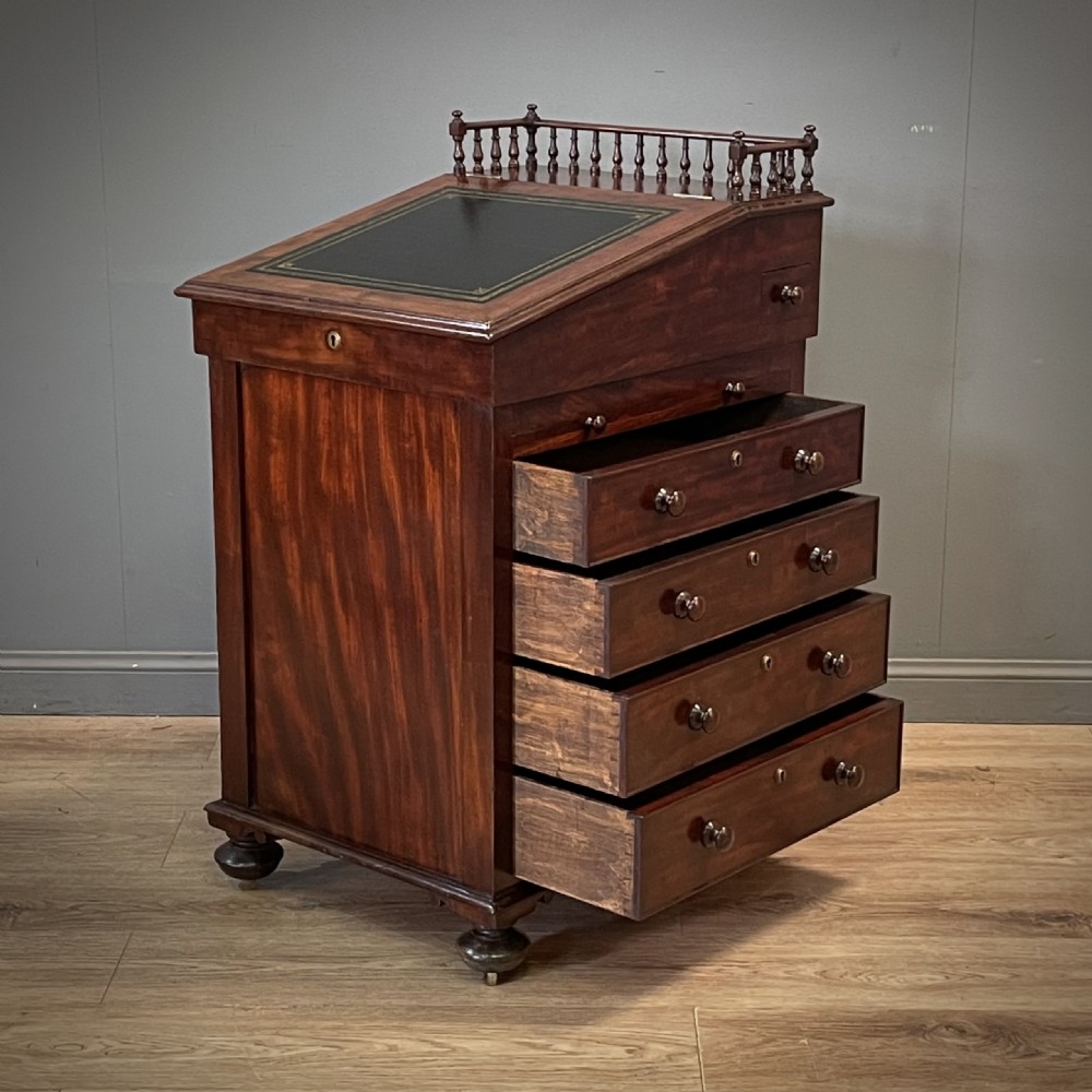 A William IV mahogany Davenport desk featuring a sloped leather writing slope, turned spindle gallery top, side drawers, and brass castors. View II