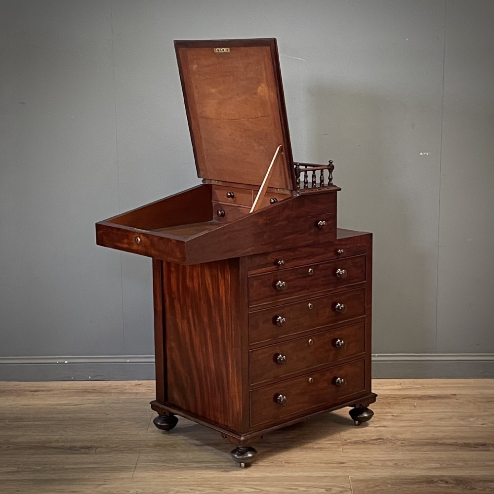 A William IV mahogany Davenport desk featuring a sloped leather writing slope, turned spindle gallery top, side drawers, and brass castors. View III